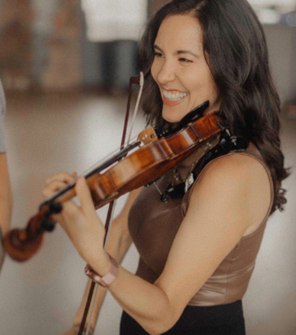 Rosie Riquelme Antunez playing the violin and smiling while performing at a wedding.